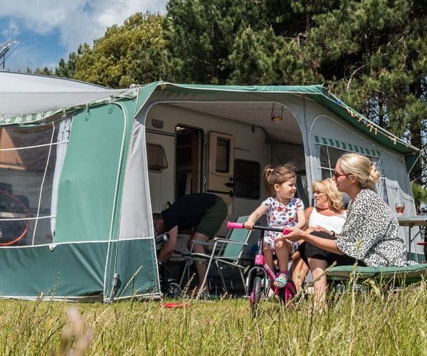 Two women and a little girl on a bike outside their awning and caravan on the Pinewoods touring park