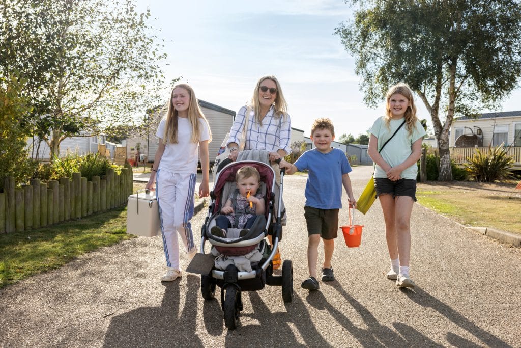 A mum pushing a baby in a pushchair walks with three children between the caravan holiday homes at Pinewoods.