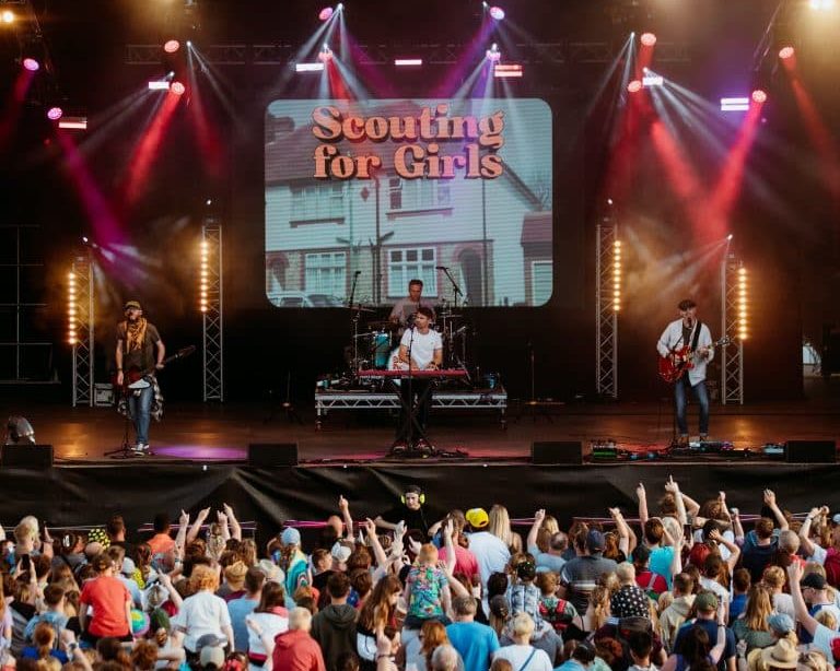 A crowd watch Scouting for Girls performing on a large lit up stage