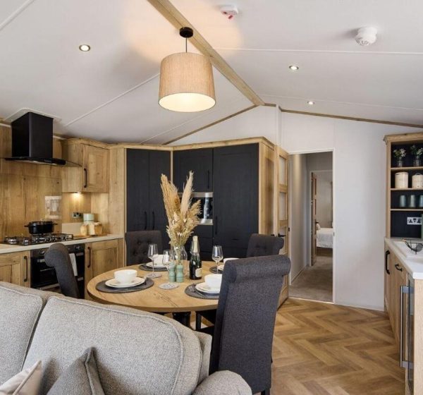 An interior shot of a modern, stylish caravan holiday home, showing the sofa and kitchen and dining spaces.