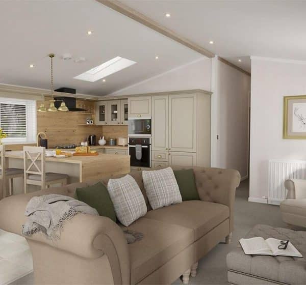 An interior shot of a holiday lodge at Pinewoods, including the lounge area with a comfy sofa and kitchen and dining area in the background.