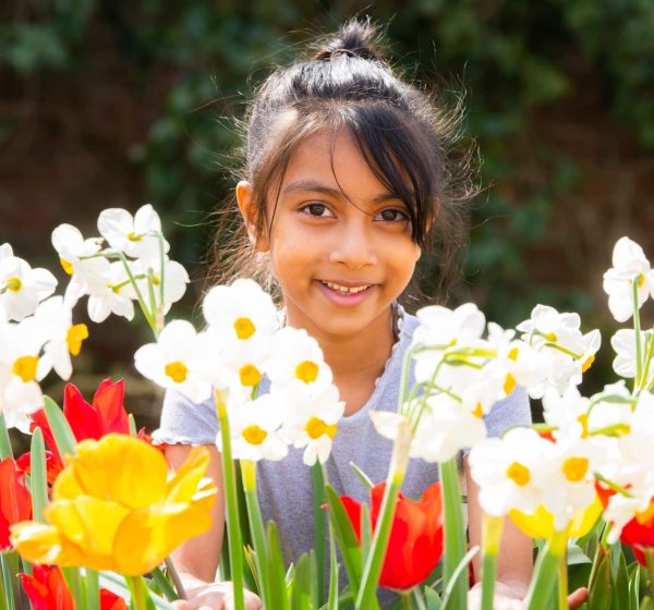 A girl smiles at the camera behind tulips and daffodils at an Easter holiday event at Holkham.